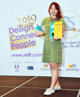 Noviaputri holding up the award and certificate won at MIFF FDC 2019